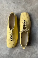 Zapato tipo flat de cuero amarillo con cordones frontales y punta cuadrada.