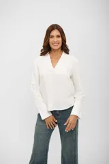 Blusa de color blanco con cuello en V y mangas largas con puños acampanados y detalle de frunces.