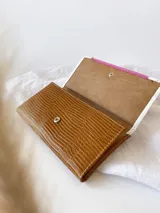 Billetera de cuero con diseño tricolor que combina texturas: cuerpo principal en marrón con textura tipo lagarto, solapa central en fucsia con textura granulada y detalles en blanco con textura tipo cocodrilo. Incluye una etiqueta central de cuero en color tostado con la marca grabada y cierre con broche.
