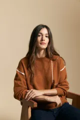 Sweater de punto color marrón con diseño de líneas blancas en contraste. Presenta cuello redondo, mangas largas y puños tejidos, con una estética minimalista y moderna.