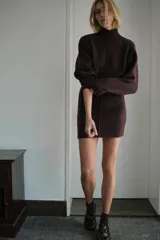 Vestido corto de punto con cuello subido, manga larga y sisa ancha. Presenta un detalle de costura vertical marcada en el centro del delantero y acabados en rib en cuello, puños y ruedo.