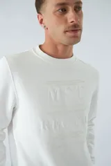 Buzo blanco de felpa con cuello redondo, mangas largas y puños. Presenta un estampado en relieve con texto y logo en goma.