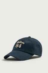 Gorra de seis paneles azul marino confeccionada en tejido de algodón, con bordado frontal en tono contrastante con la leyenda "button 84".