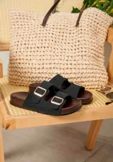 Sandalias de dos tiras negras con hebillas metálicas doradas y suela anatómica de madera oscura.