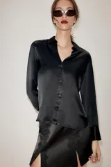 Camisa de cuello solapa y escote en pico, confeccionada en tejido satinado. Presenta manga larga con puños definidos y cierre frontal mediante botones.