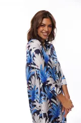Vestido camisero midi con estampado de hojas de palmera en tonos azul, blanco y negro. Tiene cuello camisero, mangas largas con puños abotonados, cierre frontal con botones y bolsillos laterales.