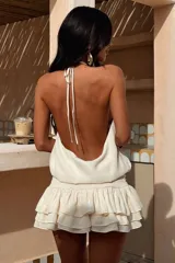 Vestido corto color beige, con escote halter, espalda descubierta y falda con volados en capas.