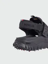 Sandalias negras con tiras ajustables de velcro, suela gruesa con tacos y detalles en rojo.