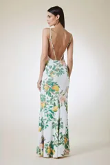 Vestido largo de silueta fluida con estampado botánico de frutas y flores sobre fondo blanco. Presenta escote en V y breteles finos con detalles metálicos.