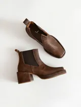 Bota tipo chelsea de cuero color chocolate con acabado texturizado, plataforma y taco cuadrado. Presenta paneles elásticos laterales en color negro.