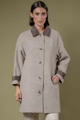 Tapado de paño en tono beige, con cuello camisero y detalles en puños en color marrón oscuro. Presenta cierre frontal con botones y bolsillos laterales.