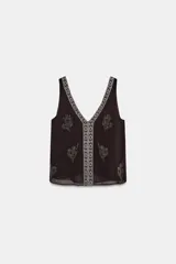 Top sin mangas color negro con escote pico profundo. Presenta bordados florales y un panel central con diseño geométrico, ambos realizados con aplicación de abalorios plateados o blancos.