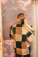 Buzo de cuero de oveja con diseño de parches cuadrados en tonos marrón, beige y verde oscuro. Presenta cuello alto con interior de piel sintética y cierre frontal.