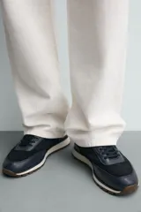 Zapatilla deportiva color verde militar, con parte superior de múltiples piezas que combinan piel y serraje. Presenta horma redonda y suela dentada en color crema con base marrón.