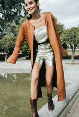 Tapado largo de cuero color marrón, abierto a los costados y en las mangas, con cuello redondo y sin botones.