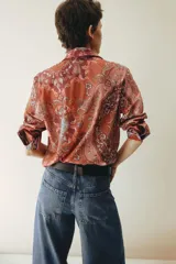 Camisa de manga larga confeccionada en gasa de algodón con estampado tipo paisley y motivos ornamentales en tonos rojizos y rosados. Presenta cuello clásico, cierre frontal con botones y puños abotonados.