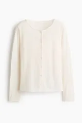 Saco entallado de punto suave, color blanco, con cuello redondo y cierre frontal de botones. Incorpora un panel interior cosido con efecto de top lencero con escote en V y ribete de encaje, creando un diseño de superposición.
