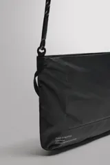Bandolera deportiva de tejido técnico color negro, con diseño plegable y compartimento principal con cierre de cremallera. Incluye bolsillo frontal con cierre, asa de hombro ajustable con cordón técnico y detalle de logo estampado.