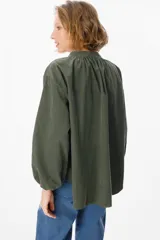 Camisa de pana color verde oliva, con cuello mao, cierre frontal de botones y mangas largas abullonadas con puños elásticos.