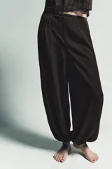 Pantalón bombacho de color marrón oscuro, confeccionado en lyocell 100%. Presenta tiro medio con cintura elástica, pliegues frontales, detalle de encaje a tono en el lateral y bajo abullonado con elástico.