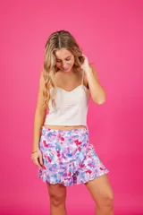 Short con diseño de pollera, tiro medio, estampado floral en tonos violeta, azul y rosado. Presenta detalle de aro de madera en la cintura, cierre lateral oculto y volados en la parte inferior.