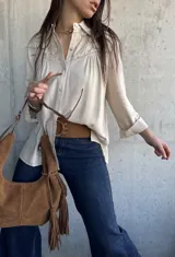 Camisa de color beige, con mangas largas y detalles bordados en el pecho y los hombros. Presenta cierre frontal con botones y cuello camisero.