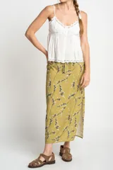 Falda midi color verde oliva con estampado de ramas en negro y blanco. Tiene corte evasé, cintura alta con cordón ajustable y abertura lateral.