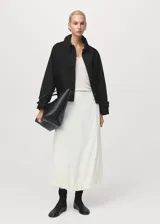 Chaqueta corta de estilo oversize en color negro, con cuello camisero, cierre frontal de botones y mangas largas con trabillas ajustables. Cuenta con dos bolsillos laterales y forro interior.