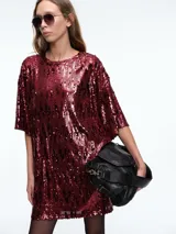 Vestido corto tipo remerón de corte oversize, confeccionado en tejido cubierto de lentejuelas brillantes. Presenta cuello redondo, mangas cortas amplias y una caída relajada.