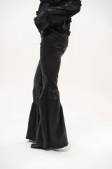 Pantalón negro de tiro medio, corte oxford, con bolsillos laterales y cierre frontal. Destaca por su diseño ajustado en la parte superior y volados fruncidos a partir de la rodilla que aportan volumen y movimiento.