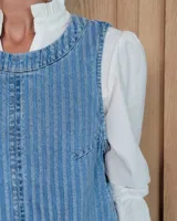 Chaleco de corte recto y largo a la cintura, confeccionado en denim con estampado de rayas verticales en tonos azul y blanco. Presenta cuello redondo y costuras visibles que definen su estructura.