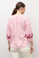 Blusa de manga larga con estampado de rayas verticales en tonos celestes y blancos. Presenta un escote en V con cierre frontal de botones y detalles de bordados florales en color crema en el frente y en los puños.