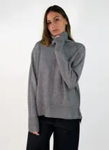 Sweater de punto gris con cuello alto, manga larga con puños acanalados y diseño holgado con costura central vertical.