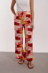 Pantalón de tiro alto, corte ancho y recto, con cordón ajustable en la cintura. Presenta un estampado abstracto en bloques de color rojo, amarillo y blanco.
