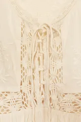 Top sin mangas color crudo, con escote en V y cierre frontal con lazos. Presenta bordados florales y detalles de encaje.