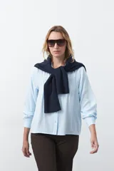 Camisa de manga larga en color celeste, con diseño de corte relajado, cuello clásico y detalle de tablas verticales en el frente.