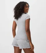 Pijama corto de dos piezas de la marca Lov, confeccionado en tejido peach touch de poliéster y elastano. Incluye una remera de manga corta con escote redondo, detalle de frunce en el busto y terminaciones con volados, acompañada de un short con cintura elástica y diseño estampado a cuadros vichy en tonos gris y blanco.
