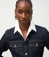 Campera de jean color azul oscuro, con diseño entallado, cuello camisero, mangas largas con puños abotonados y cierre frontal con botones metálicos. Presenta recortes estructurales que realzan la silueta.
