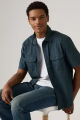 Camisa de manga corta color azul petróleo, con cuello clásico, cierre frontal con botones, dos bolsillos de parche con botón en el pecho y corte recto.