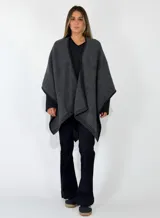 Ruana de tejido de punto en color gris oscuro, con diseño abierto y bordes acanalados. Presenta una caída fluida y holgada, ideal para superponer sobre otras prendas.