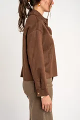 Sobrecamisa oversize de gamuza vegana marrón, con cuello camisero, mangas largas y cierre frontal de botones metálicos.