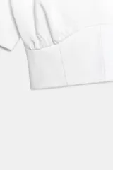 Camiseta corta blanca de manga corta y cuello redondo, estilo corsetero con parte inferior ajustada.