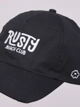 Gorro de visera negro de lona, con bordado frontal en blanco que dice "Rusty Beach Club" y un pequeño bordado de flor en el lateral.