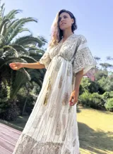 Túnica larga de estilo boho, color crudo con estampado de arabescos y detalles en hilo dorado. Presenta escote en V, mangas amplias tipo kimono y cordón ajustable en la cintura con borlas decorativas.