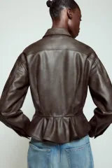 Cazadora de efecto piel con cuello solapa, manga larga y cierre frontal con botones. Presenta falsos bolsillos con solapa en el delantero y bajo con acabado peplum.