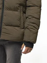 Campera puffer color verde militar, con diseño capitoneado, cuello alto y capucha integrada. Cuenta con cierre frontal, bolsillos laterales con cierre y puños con ojal para el pulgar.