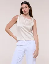 Blusa de satén beige con escote asimétrico drapeado y detalle de aro metálico en el hombro.