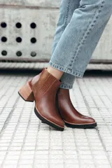 Bota corta de cuero color marrón, con diseño de texturas combinadas en los laterales y elástico. Presenta un taco medio de madera y suela de goma negra.