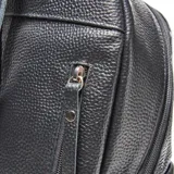 Mochila de cuero negro con textura granulada, cierre principal con doble tirador y bolsillo frontal con placa metálica plateada con logo XL.