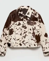 Campera con estampado de vaca en tonos marrón y blanco, de corte recto, con cuello camisero, cierre con botones a presión, bolsillos de parche en el pecho y bolsillos laterales.